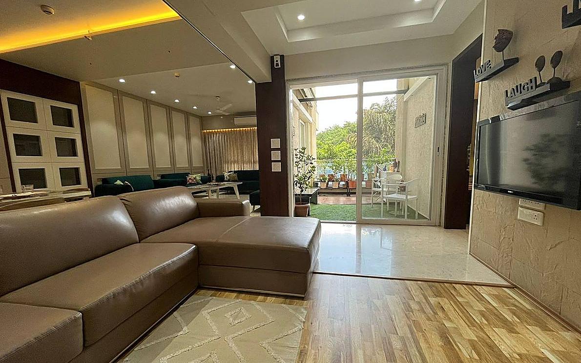 The Kogta House - living room with a tan leather sectional, wooden floor and a glass door opening to a green balcony